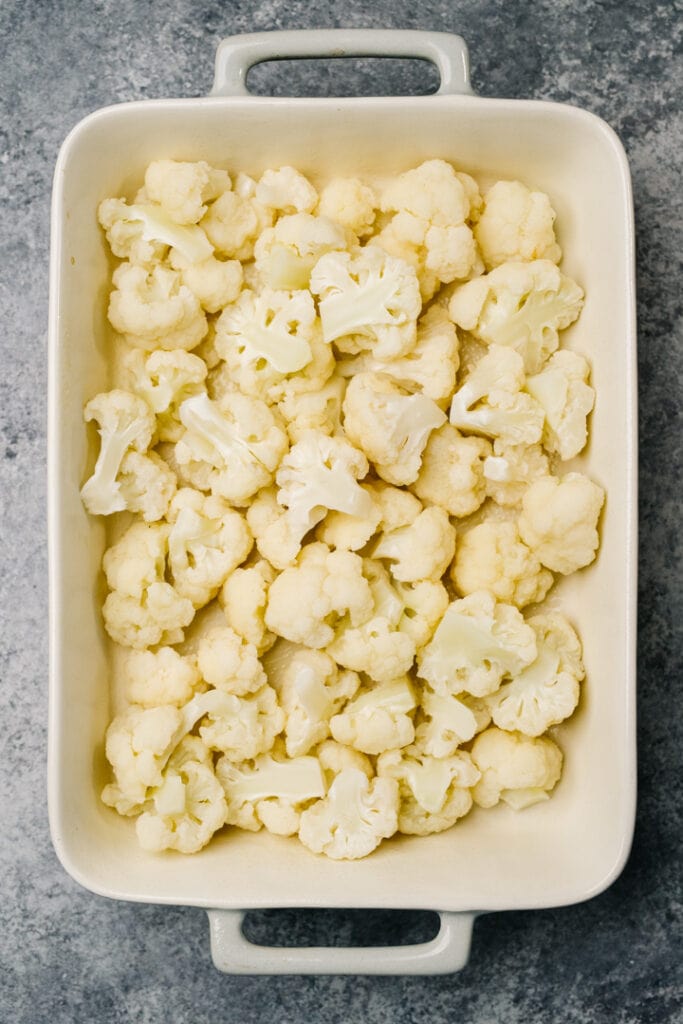 Steamed cauliflower florets arranged in a greased casserole dish.