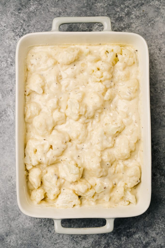 Cauliflower florets tossed with cheesy bechamel sauce in a casserole dish.