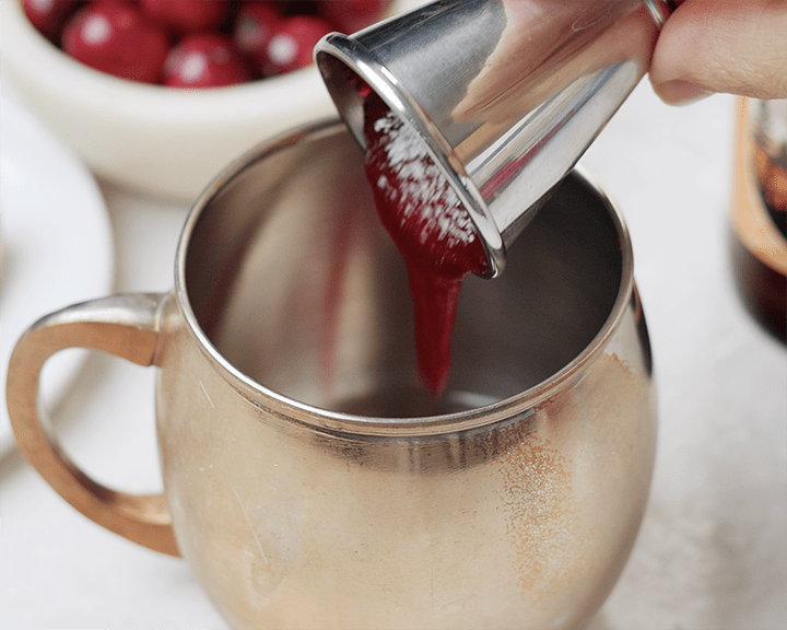 Pouring homemade cranberry syrup into a copper mug.