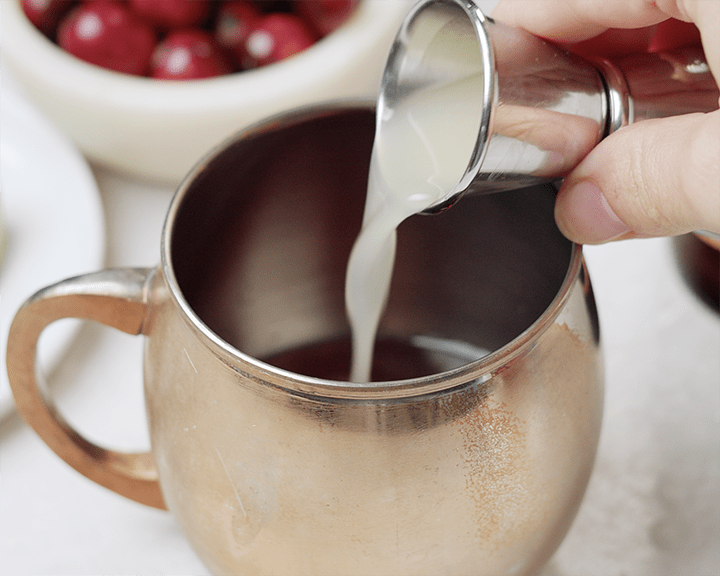 Adding lime juice to a copper mug with vodka and cranberry syrup.