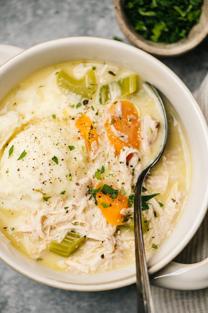 A silver soup spoon tucked into a bowl of creamy leftover turkey stew, served over mashed potatoes.