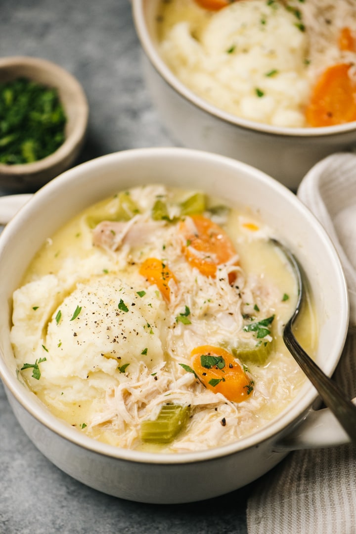 Two bowls of creamy turkey soup made with Thanksgiving leftovers on a concrete surface with a cream linen napkin to the side.