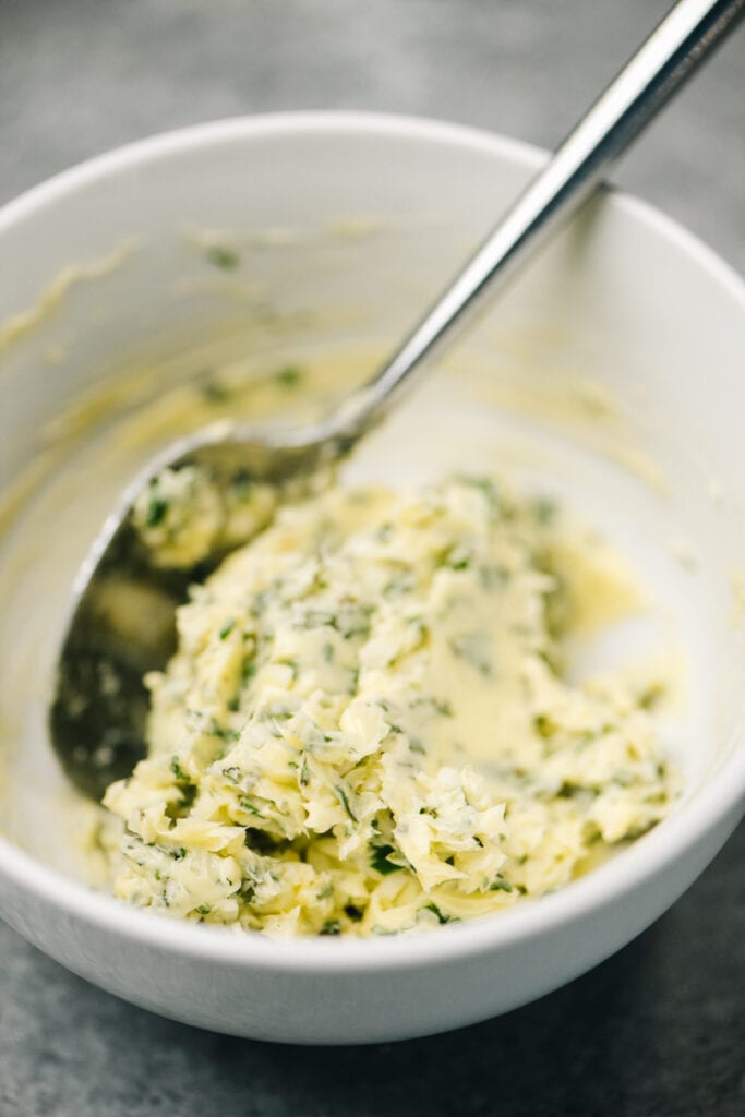 Softened butter mixed with fresh herbs and garlic in a small white bowl.