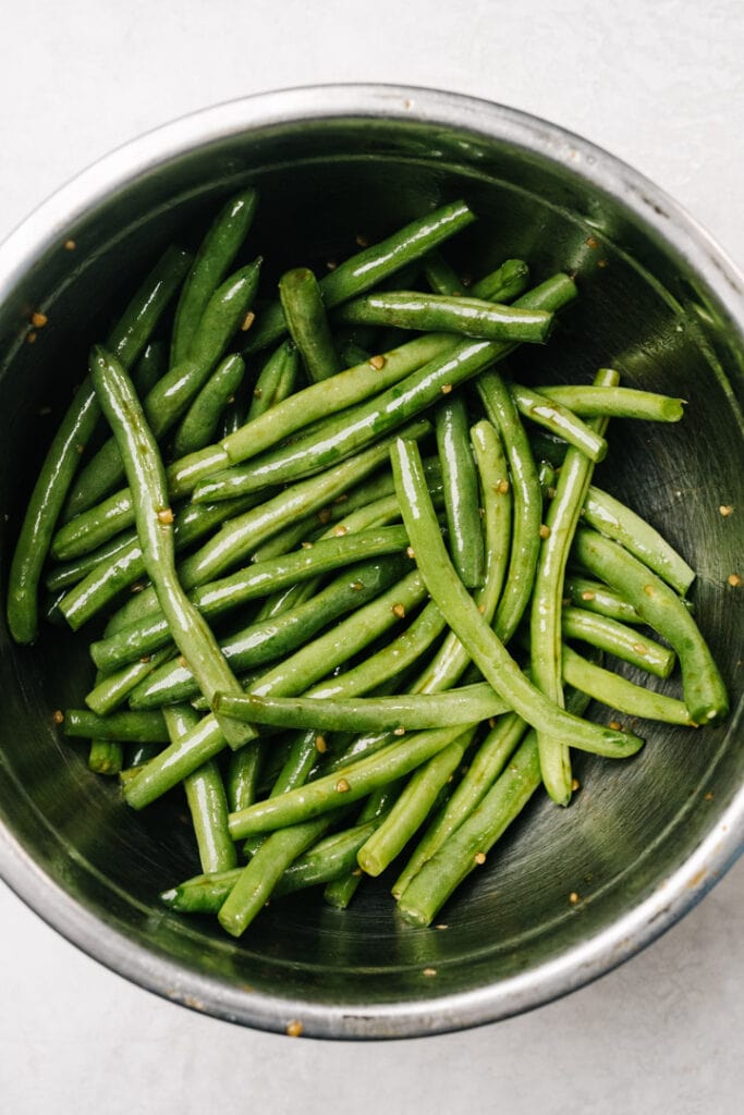 Fresh green beans tossed with a mixture of butter, olive oil, balsamic vinegar, soy sauce, and minced garlic in a metal mixing bowl.
