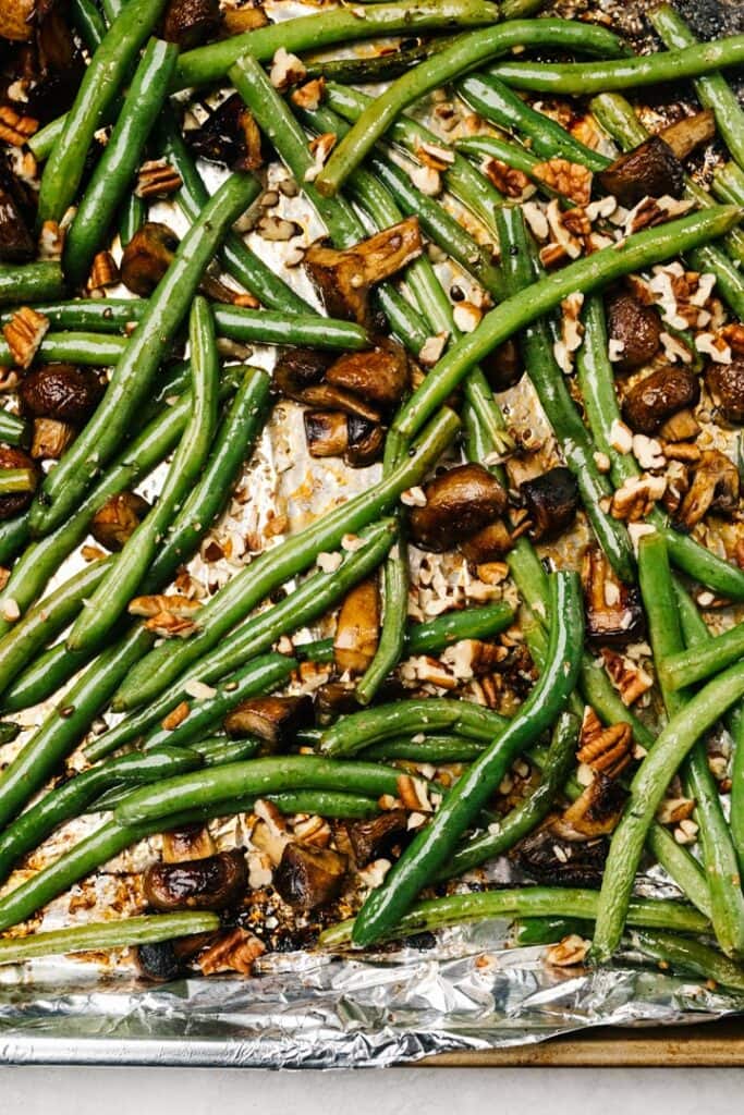 Roasted mushrooms and green beans on a foil lined baking sheet garnished with chopped pecans.