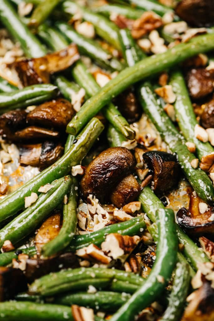 Side view, roasted mushrooms and green beans with pecans on a foil lined baking sheet.