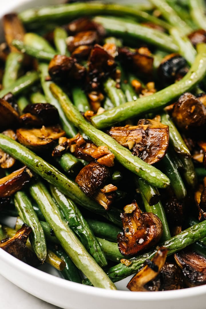 Side view, roasted green beans and mushrooms in a white serving bowl.