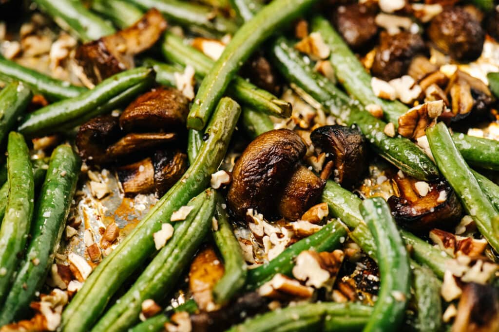 Side view, roasted mushrooms and green beans with pecans on a foil lined baking sheet.