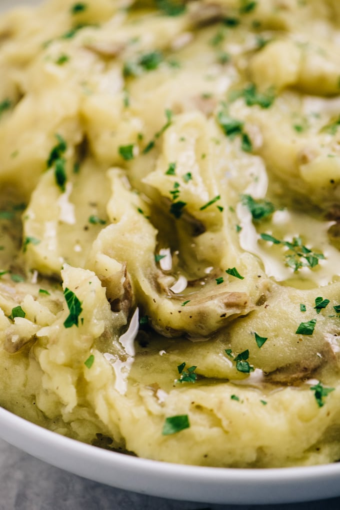 Side view, healthy mashed potatoes in a white bowl garnished with more olive oil and chopped parsley.