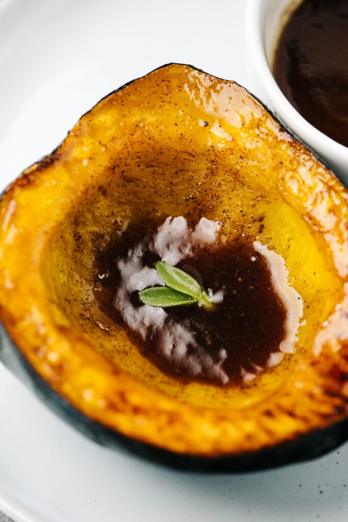 Side view, a roasted acorn squash half drizzled with maple browned butter.