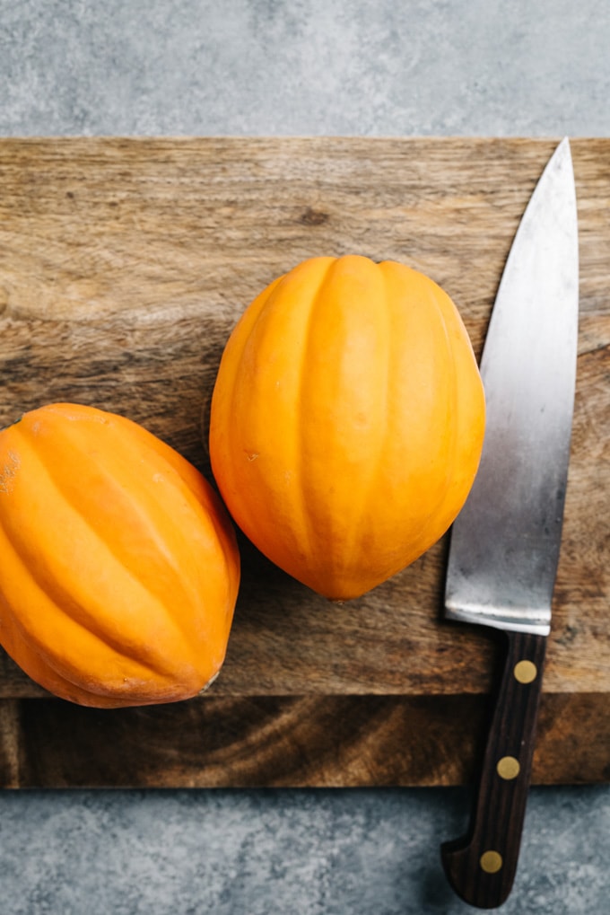 Two acorn squash on a cutting board with a chef's knife.