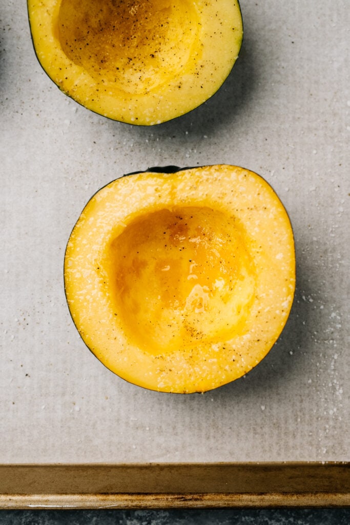 Acorn squash halves rubbed with olive oil and seasoned with salt and pepper on a parchment lined baking sheet.