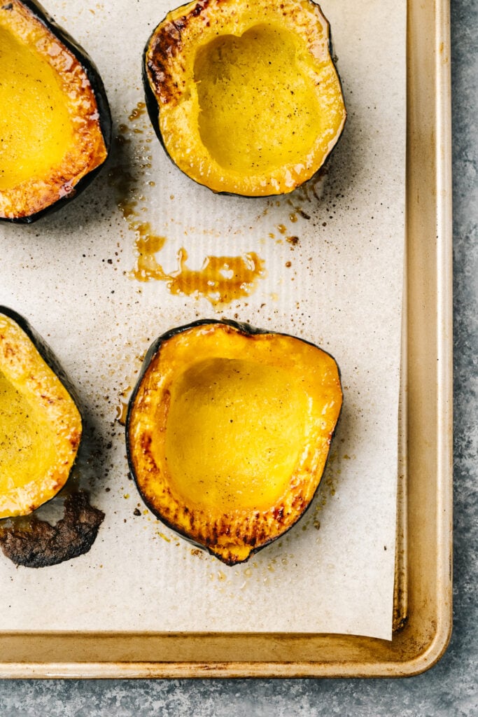 Roasted acorn squash halves on a parchment lined baking sheet.