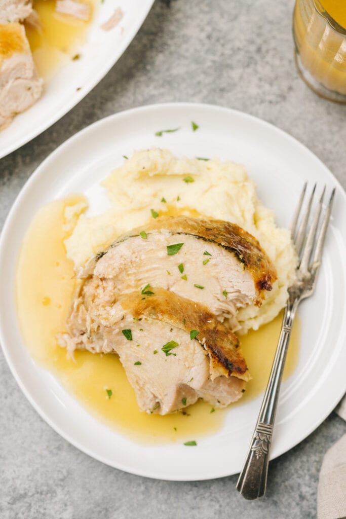 Sliced instant pot turkey breast over mashed potatoes on a white plate with gravy and a silver fork.
