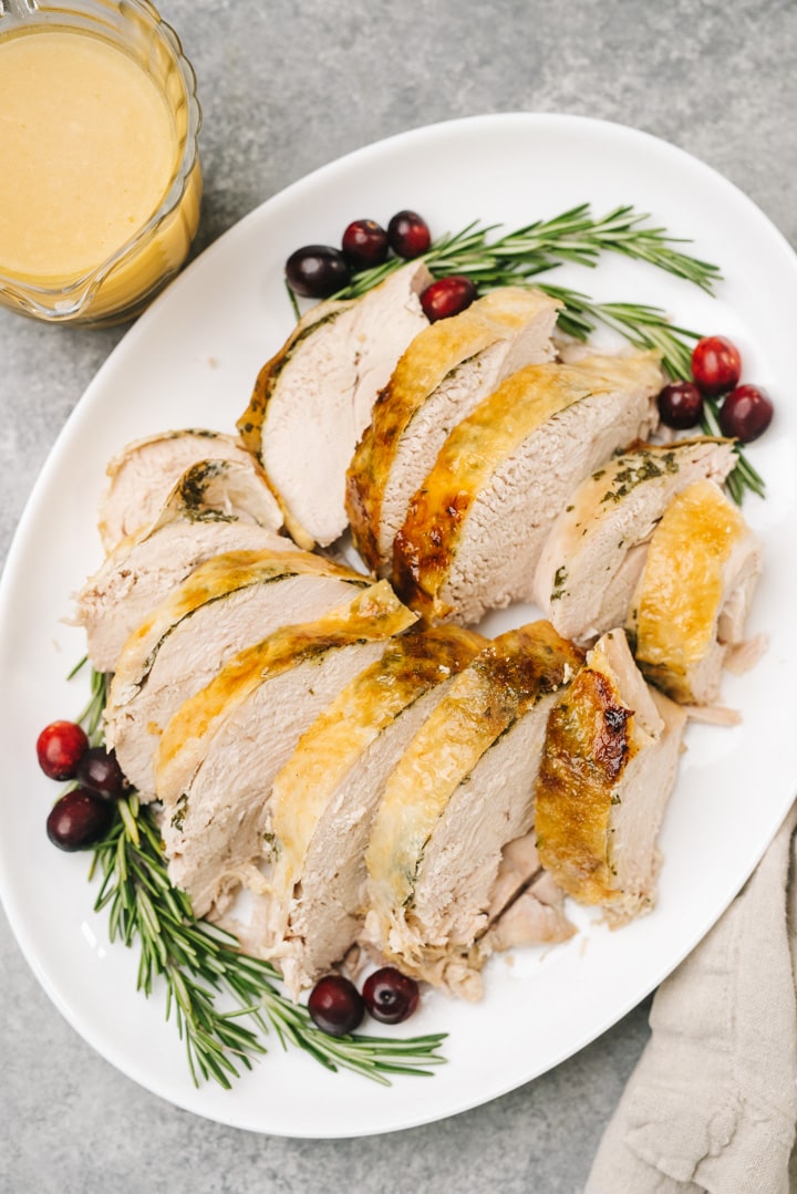 Sliced pressure cooker turkey breast on a white platter, garnished with fresh herbs and cranberries.