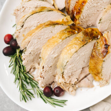 Slices of instant pot turkey breast on a white platter, garnished with fresh cranberries and rosemary sprigs.
