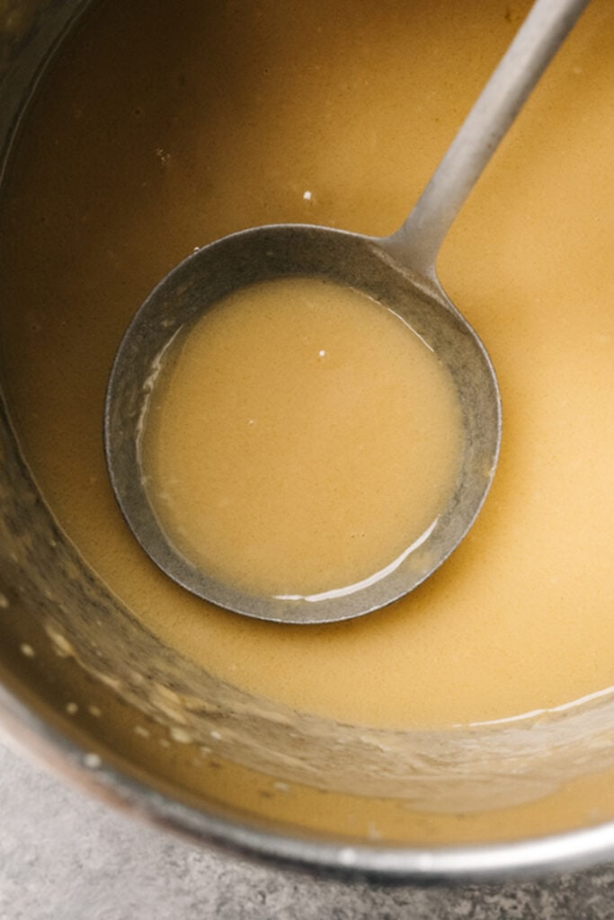 A ladle dipped into a saucepan full of gravy.