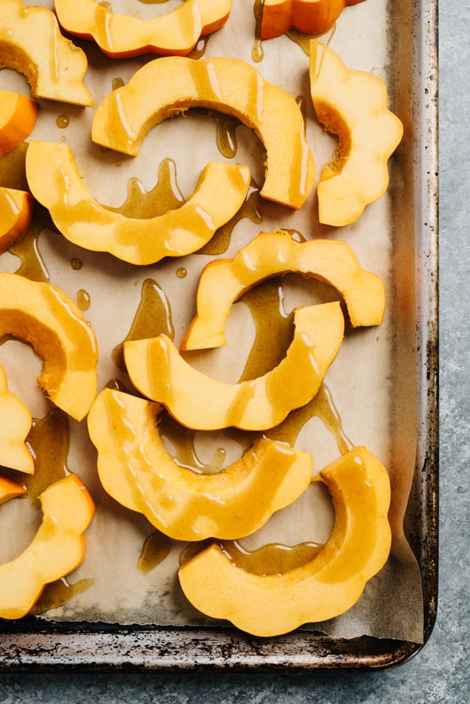 Sliced acorn squash drizzled with maple browned butter on a parchment lined baking sheet.