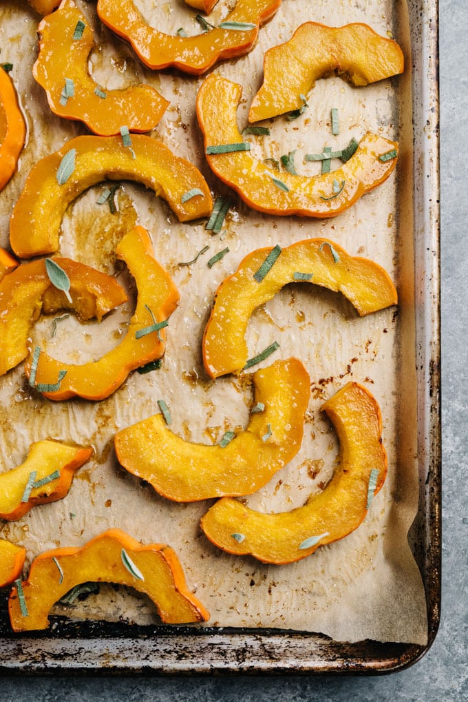 Roasted acorn squash slices on a parchment lined baking sheet, garnished with fresh sage.