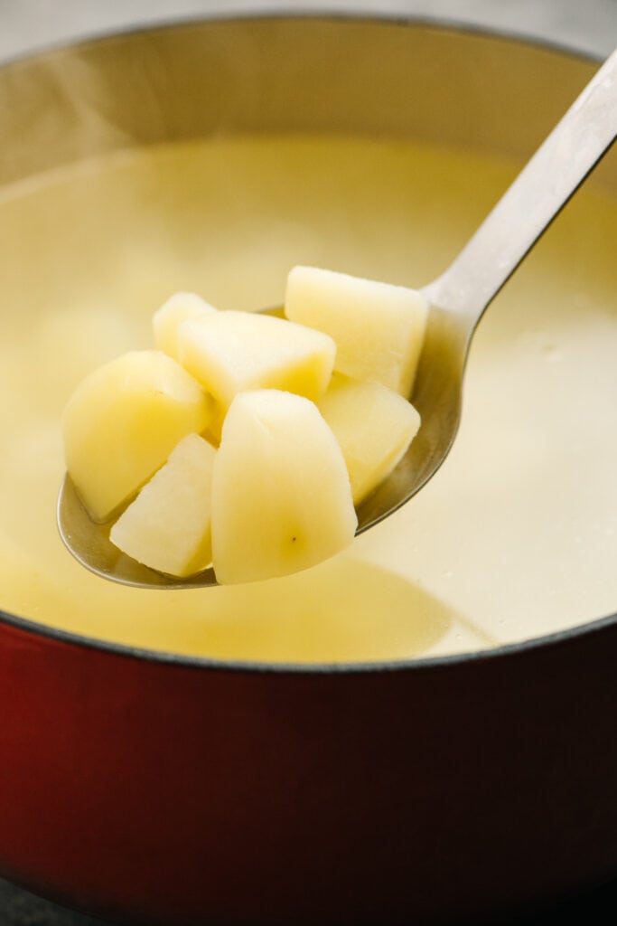 Cooked diced potatoes in a slotted spoon hovering over a pot.