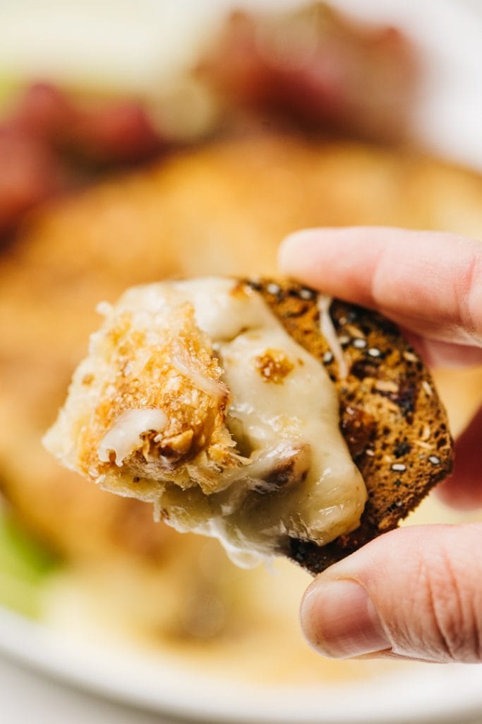 A woman's hand holding a cracker topped with baked brie.
