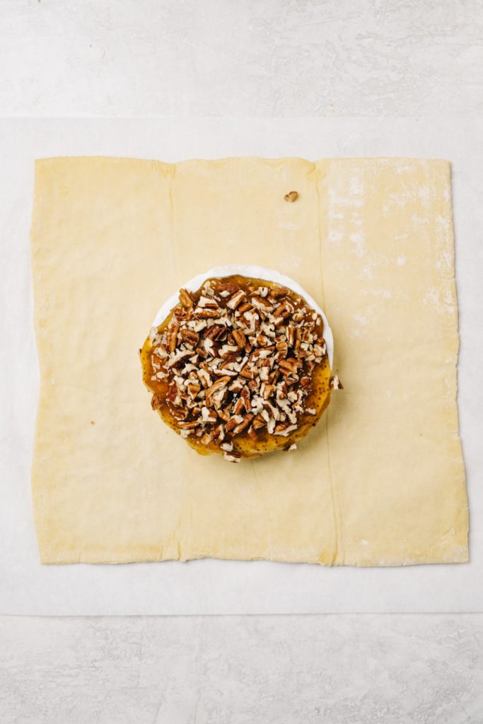 A wheel of brie topped with fig jam and pecans on a piece of rolled out puff pasty.