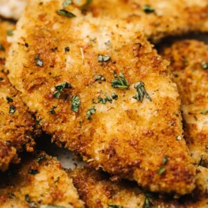 Side view, several parmesan crusted chicken breasts on a tan speckled serving platter.