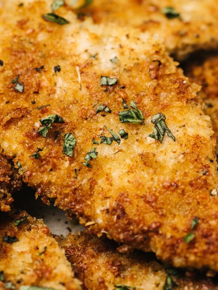 Side view, several parmesan crusted chicken breasts on a tan speckled serving platter.