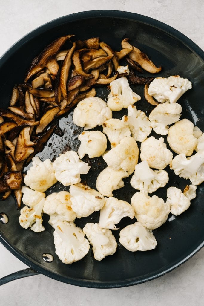 Stir fried cauliflower and mushrooms in a skillet.