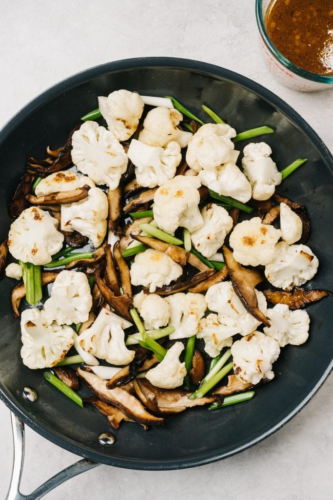 Stir fried cauliflower, mushrooms, and green onions in a large skillet.