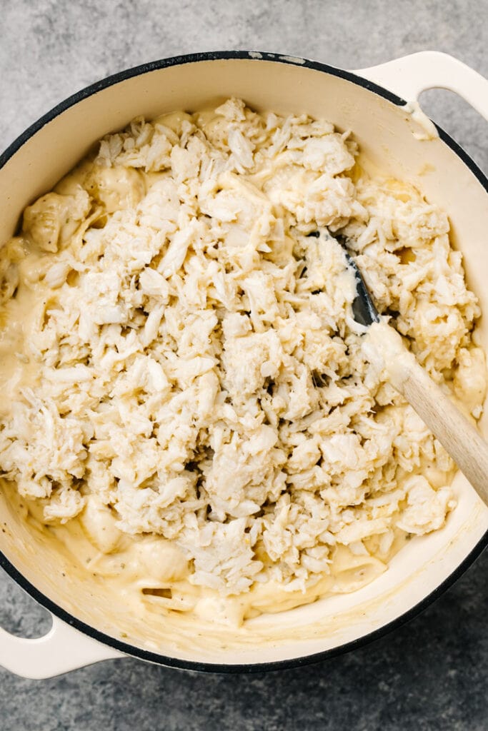 Folding crab meat into mac and cheese in a white dutch oven.