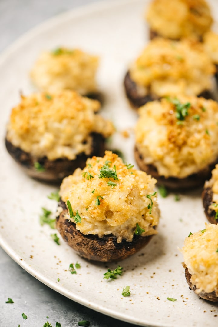 Side view, crab stuffed mushrooms on a serving platter, garnished with chopped parsley.