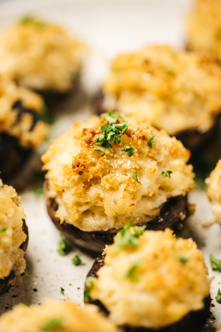 Side view, stuffed mushrooms with crab on a serving platter, garnished with chopped parsley.