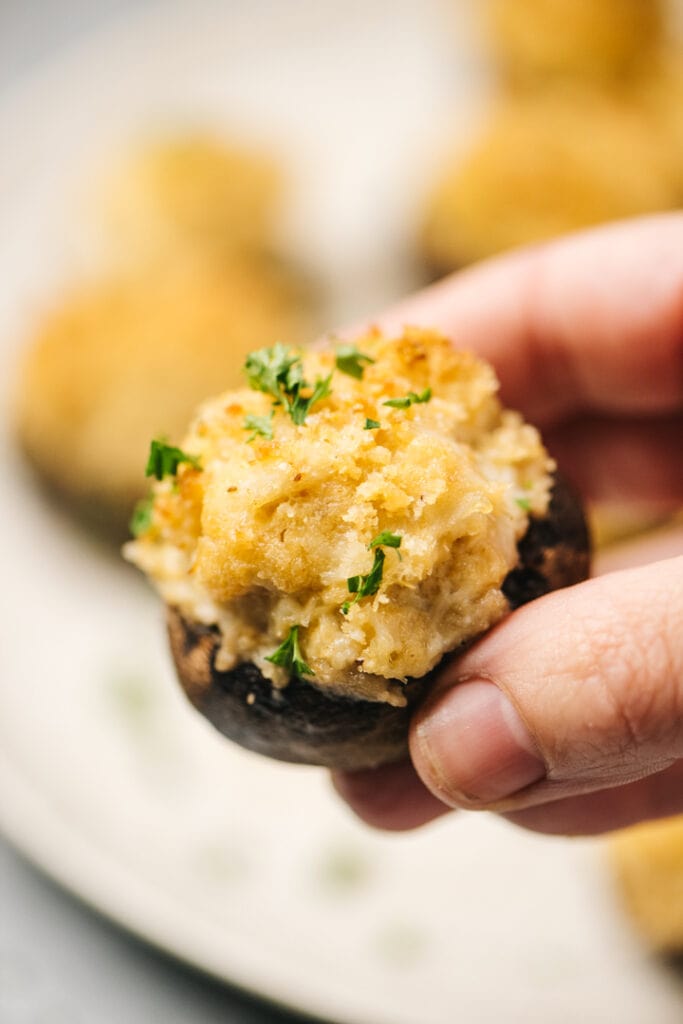 Side view, a woman's hand holding a crab stuffed mushroom.