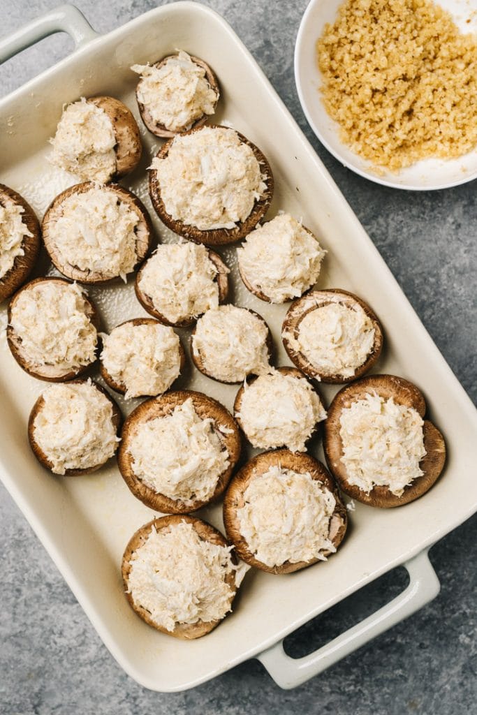 Mushrooms stuffed with crab filling in a single layer in a casserole dish.