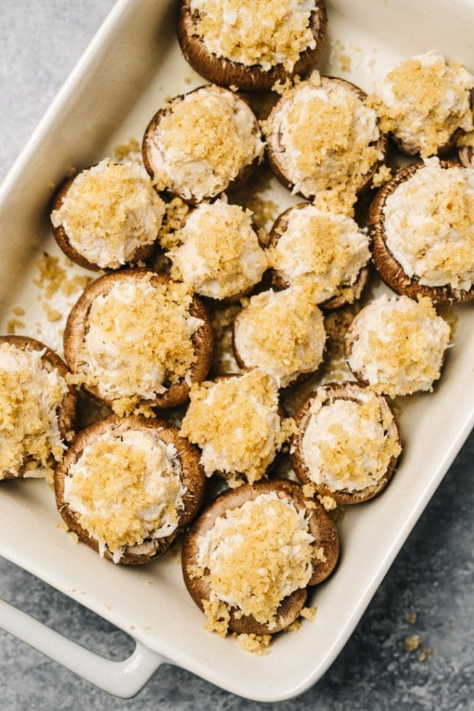 Crab stuffed mushrooms topped with breadcrumbs in a single layer in a casserole dish.