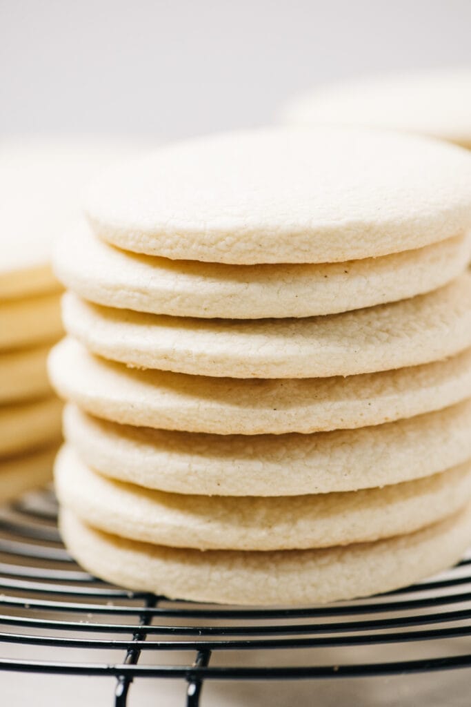 Side view, several stacks of gluten free sugar cookies on a circular black cooling rack.