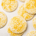Gluten free sugar cookies with icing and gold sprinkles scattered on a light concrete background.