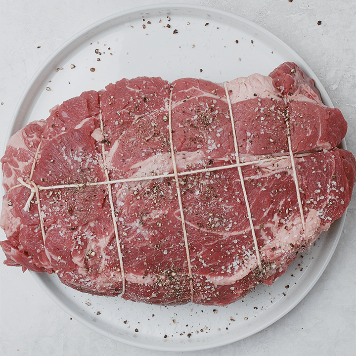 A chuck roast trussed with kitchen twine seasoned with salt and pepper.