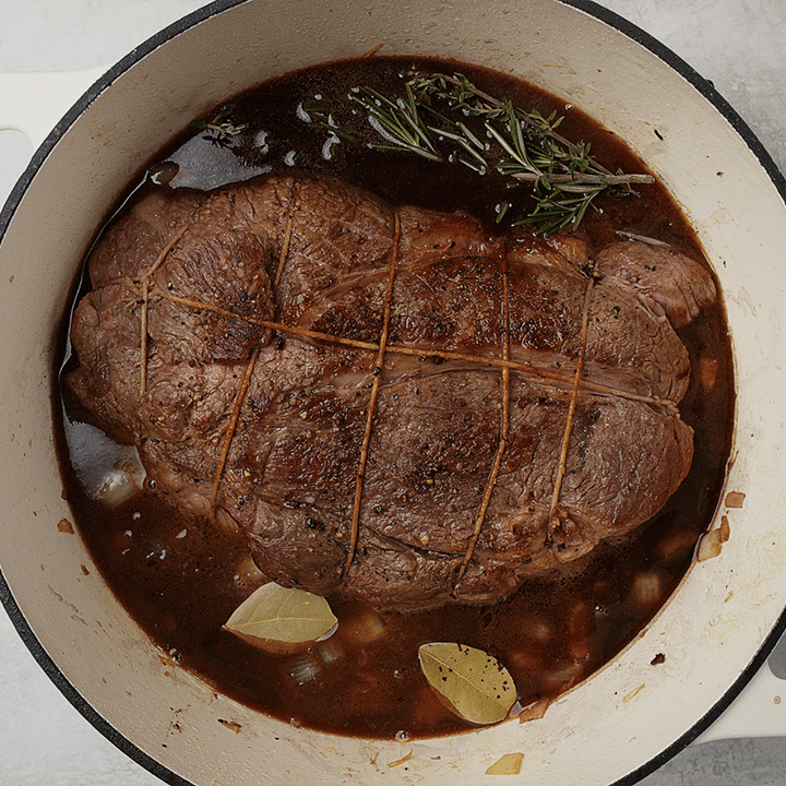 A seared chuck roasted in a dutch oven with red wine braising liquid, rosemary, thyme, and bay leaves.