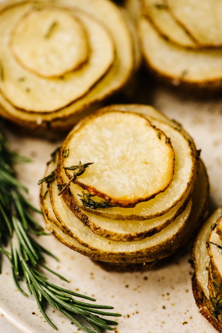 Side view, crispy herb potato stacks on a serving platter, garnished with fresh rosemary sprigs.