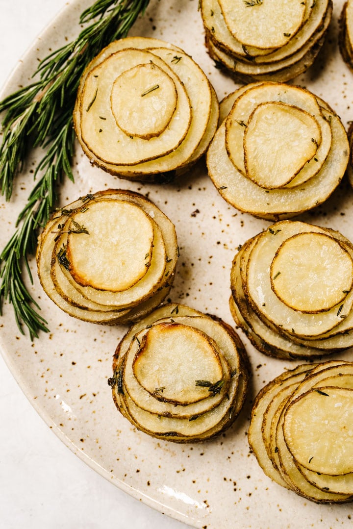 Crispy herb potato stacks on a speckled cream serving platter, garnished with fresh rosemary sprigs.