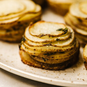 Side view, crispy potato stacks on a speckled tan serving platter.