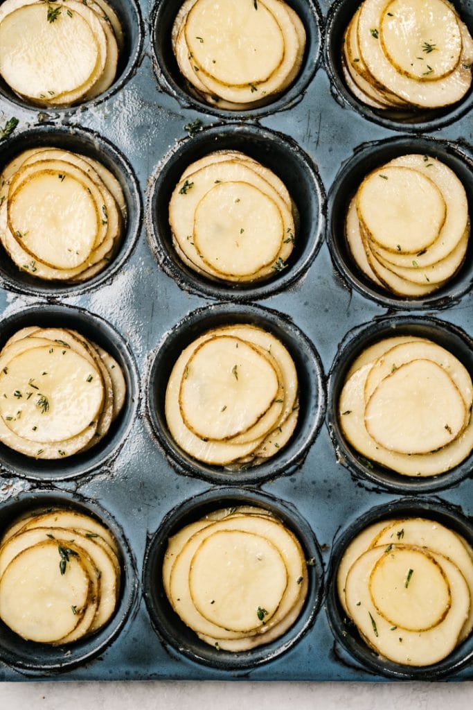 Thinly sliced potato stacks seasoned with butter and herbs in a muffin tin.