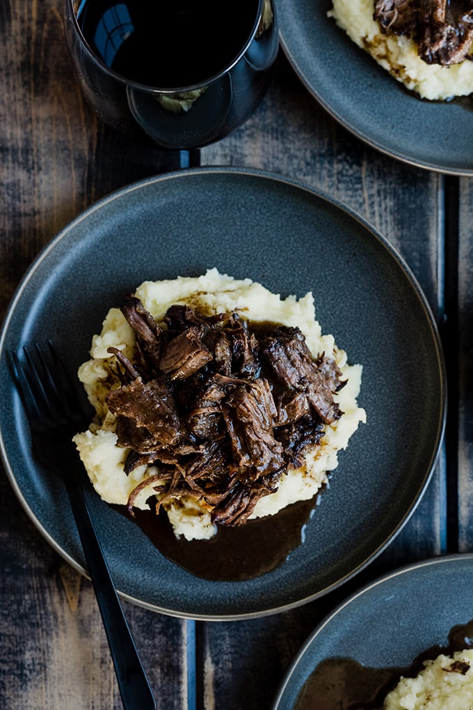 Red wine braised pot roasted over mashed potatoes on a gray plate, drizzled with plenty of au just.