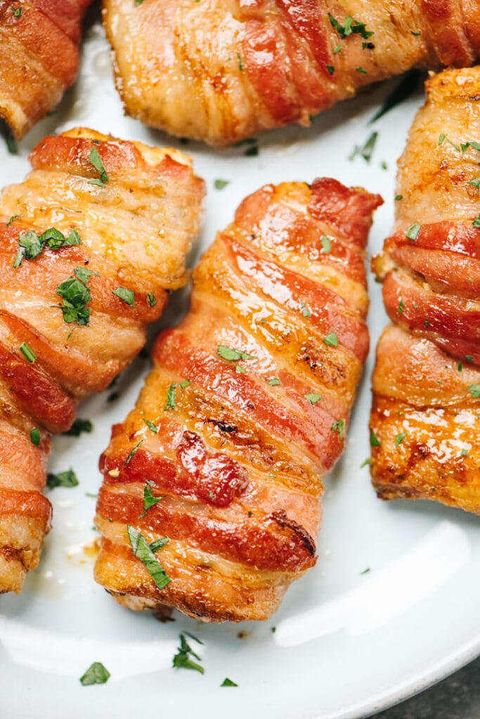 Crispy bacon wrapped chicken garnished with fresh parsley on a light blue plate.