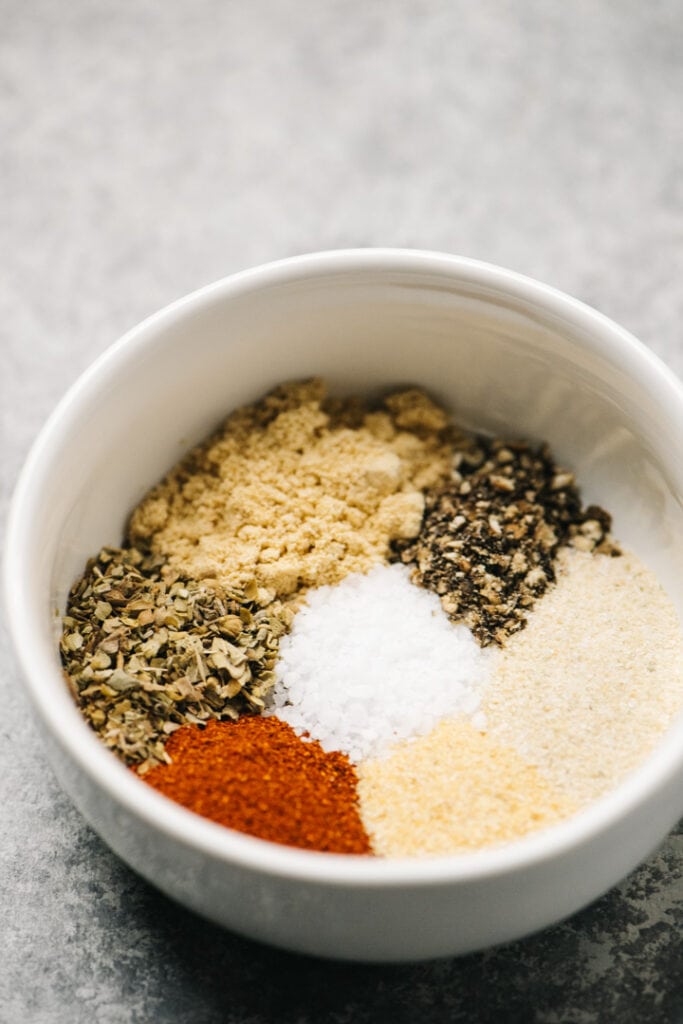 Dried herbs and spices for seasoning chicken in a small white bowl.