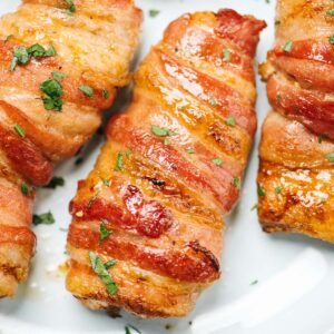 Crispy bacon wrapped chicken garnished with fresh parsley on a light blue plate.