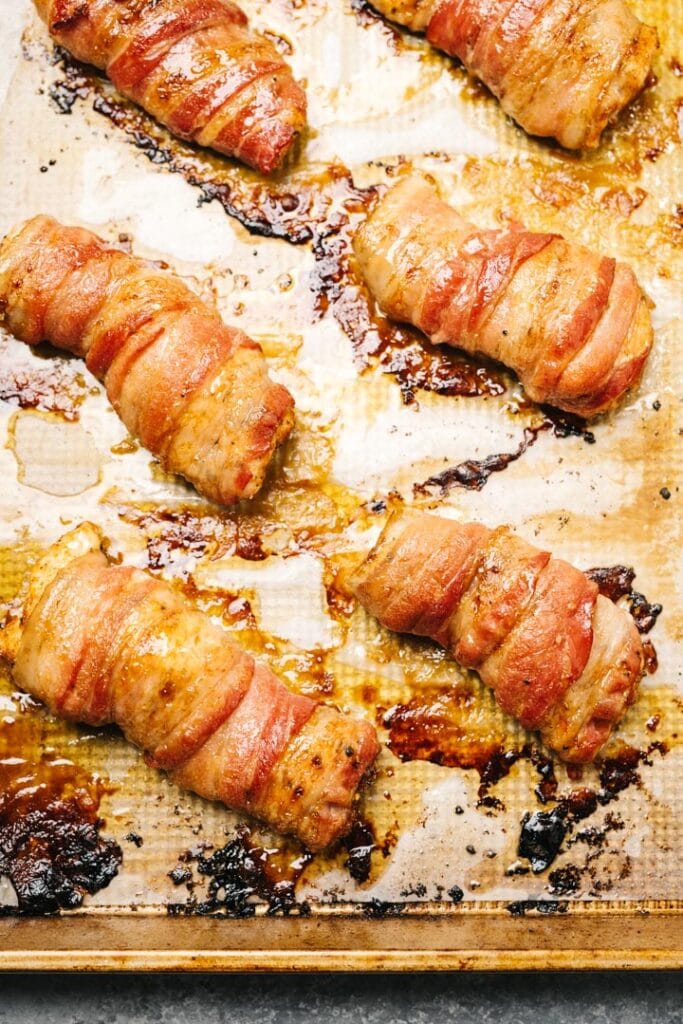 Crispy bacon wrapped chicken thighs on a parchment lined baking sheet.
