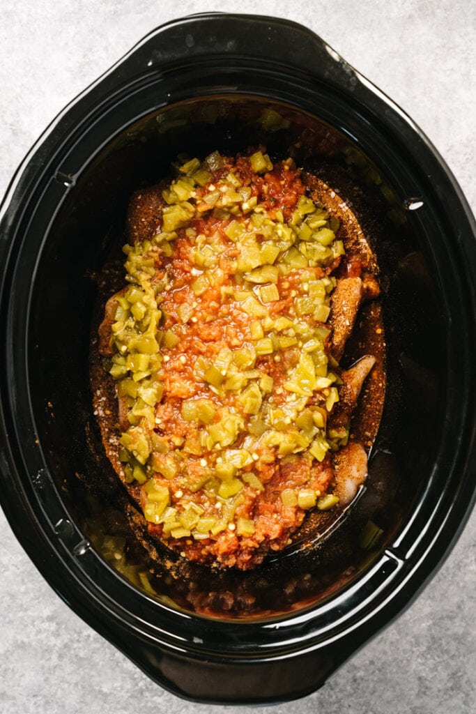 Boneless chicken breasts in a crockpot covered with taco seasoning, salsa, and green chiles.